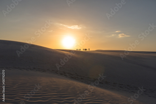 Travelers walking over sand dunes at sunset