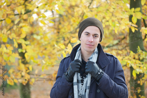 Handsome young man standing outdoors with hat scarf and gloves