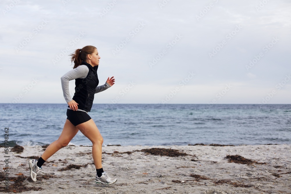 Fit and healthy young woman running along shoreline