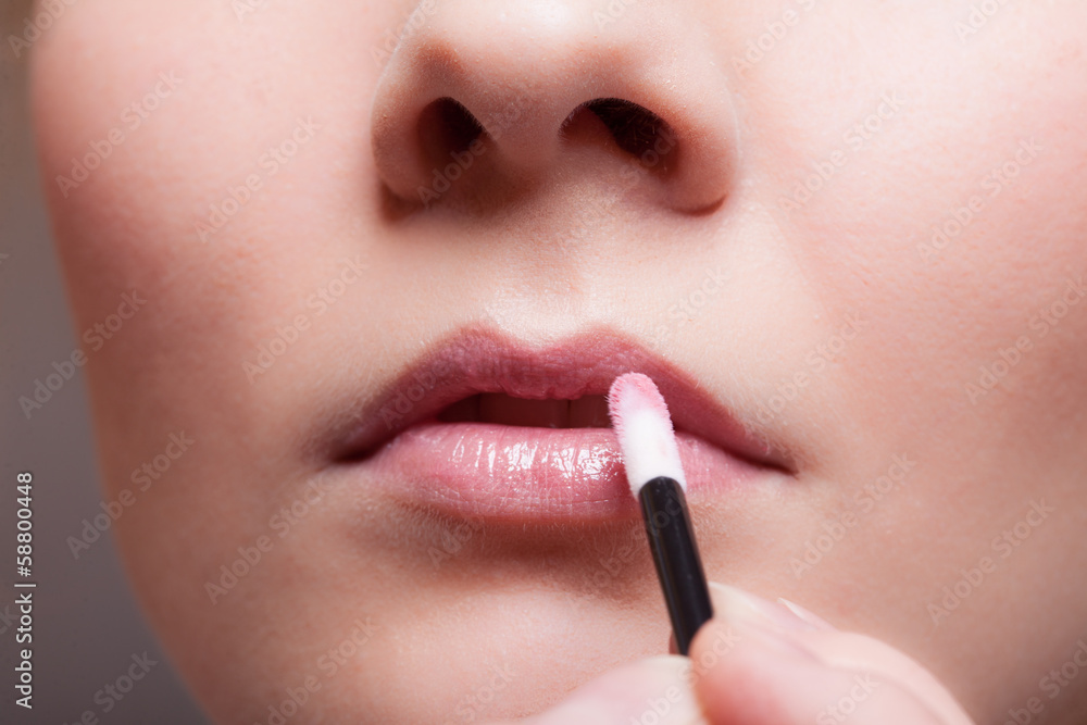 Makeup. Girl applying lipgloss lipstick on lips. Part of face.