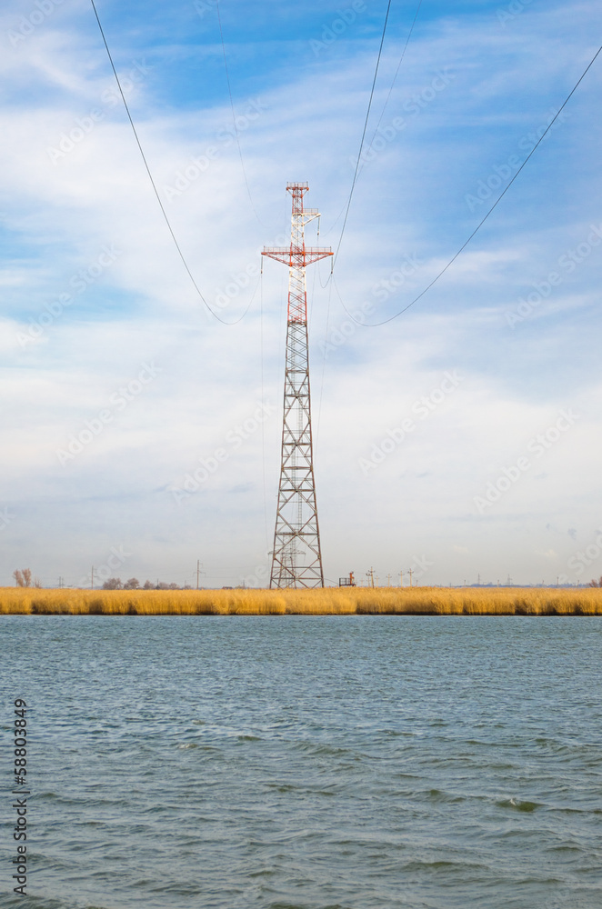 Fototapeta premium Высокая опора линии электропередачи стоит на берегу широкой реки