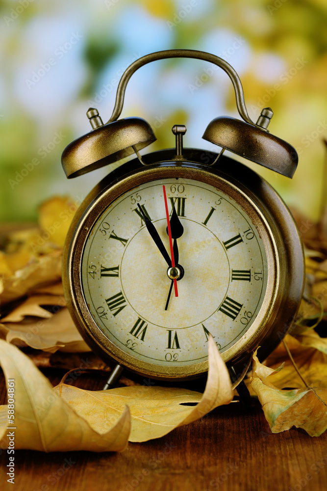 Old clock on autumn leaves on wooden table on natural Old clock on autumn leaves on wooden table on natural