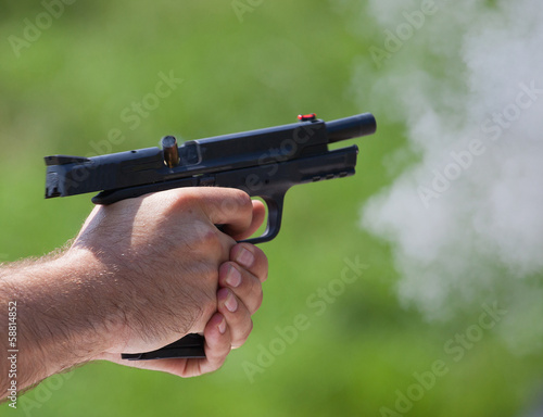 Moment of ejection as a pistol has just release a shot, smoke surrounds the barrel and brass if flying from the chamber