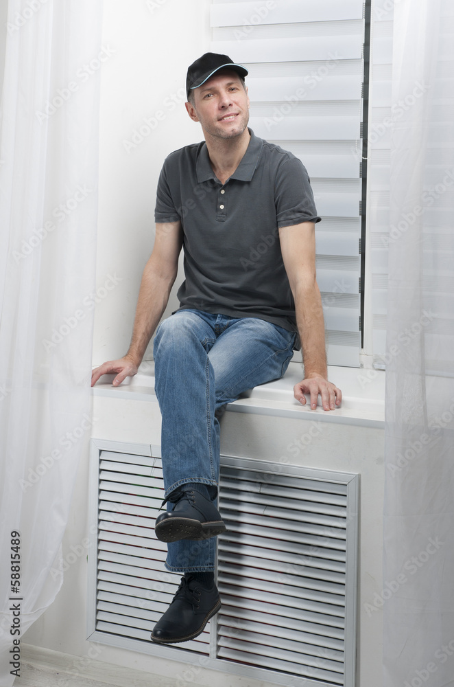 young smiling man sitting on a white window young smiling man sitting on a white window