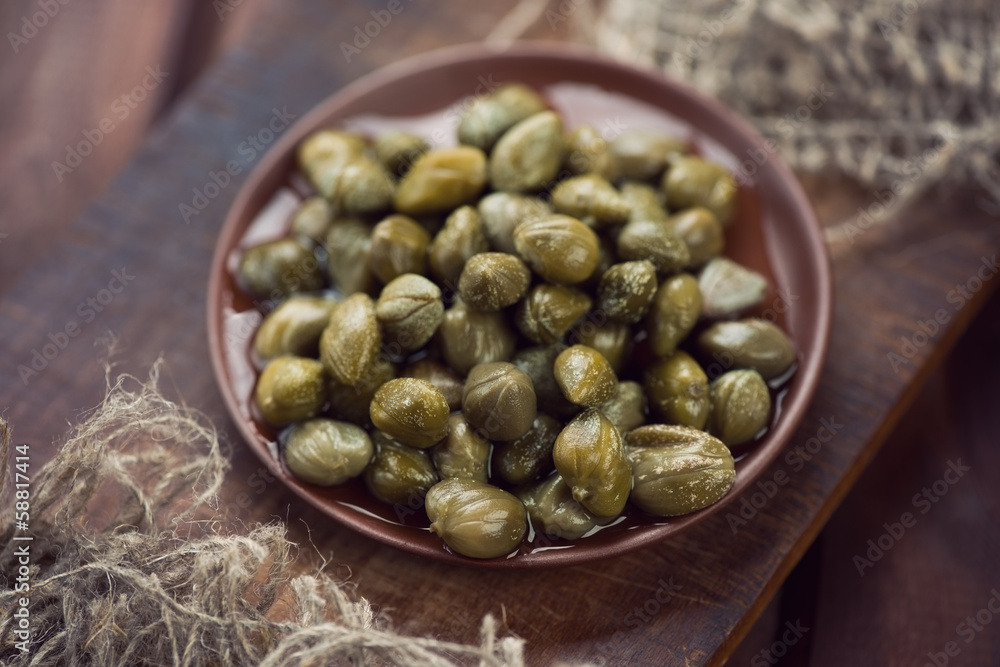 Ceramic plate with pickled capers, rustic wooden background Ceramic plate with pickled capers, rustic wooden background