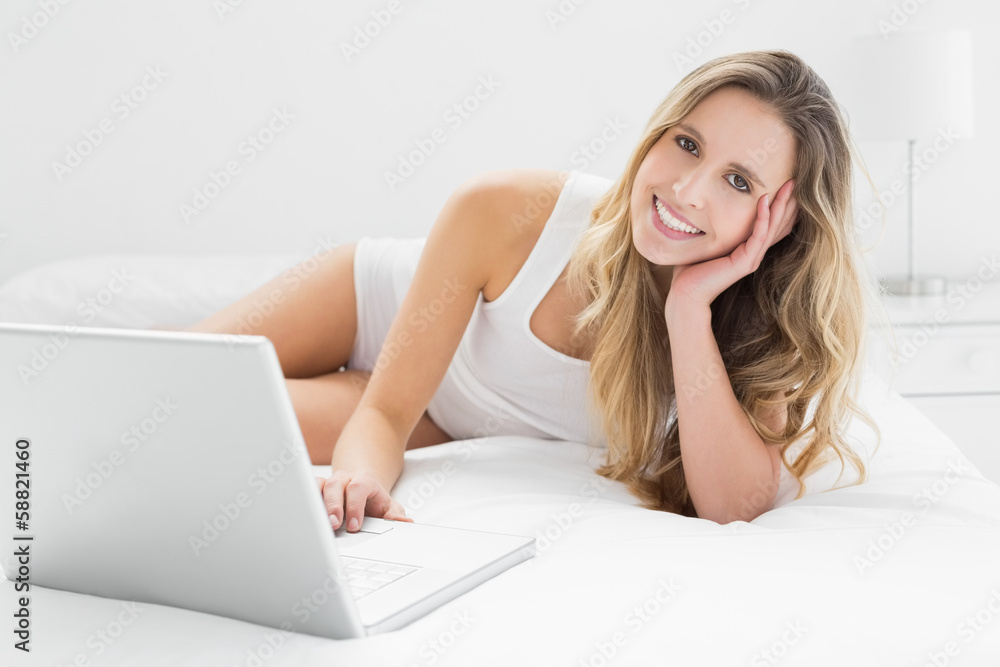 Smiling young woman using laptop in bed Smiling young woman using laptop in bed