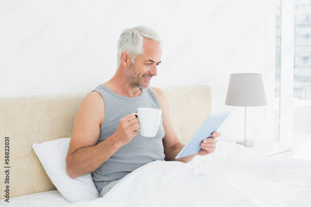 Smiling mature man with digital tablet and coffee table in bed Smiling mature man with digital tablet and coffee table in bed