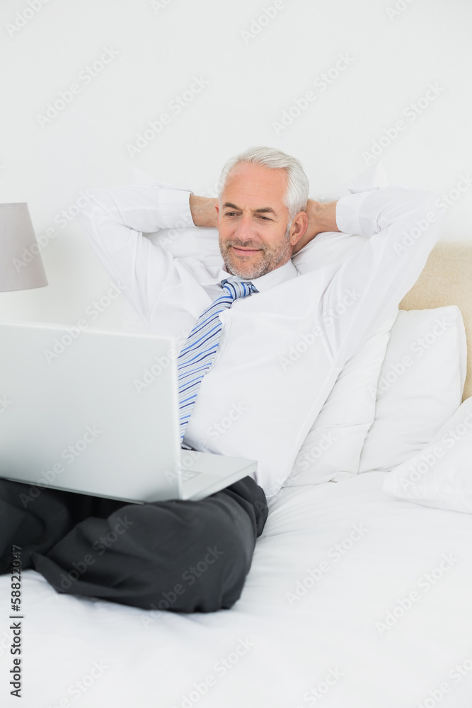 Relaxed businessman looking at laptop in bed Relaxed businessman looking at laptop in bed