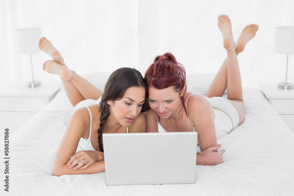 Relaxed female friends using laptop in bed Relaxed female friends using laptop in bed