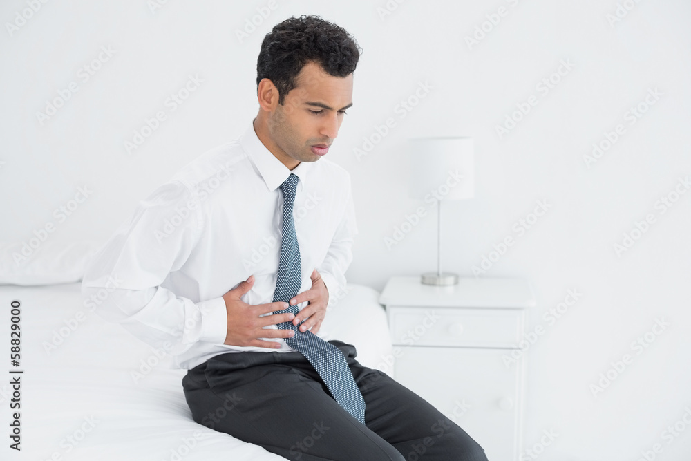 Businessman with stomach pain sitting on bed Businessman with stomach pain sitting on bed