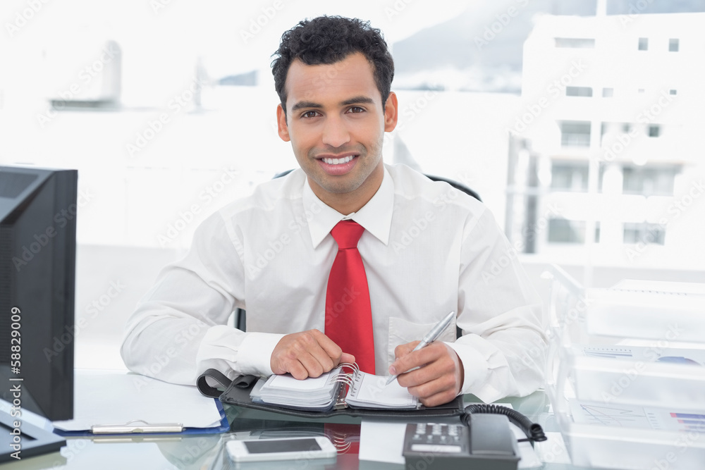 Smiling young businessman writing in diary at office Smiling young businessman writing in diary at office