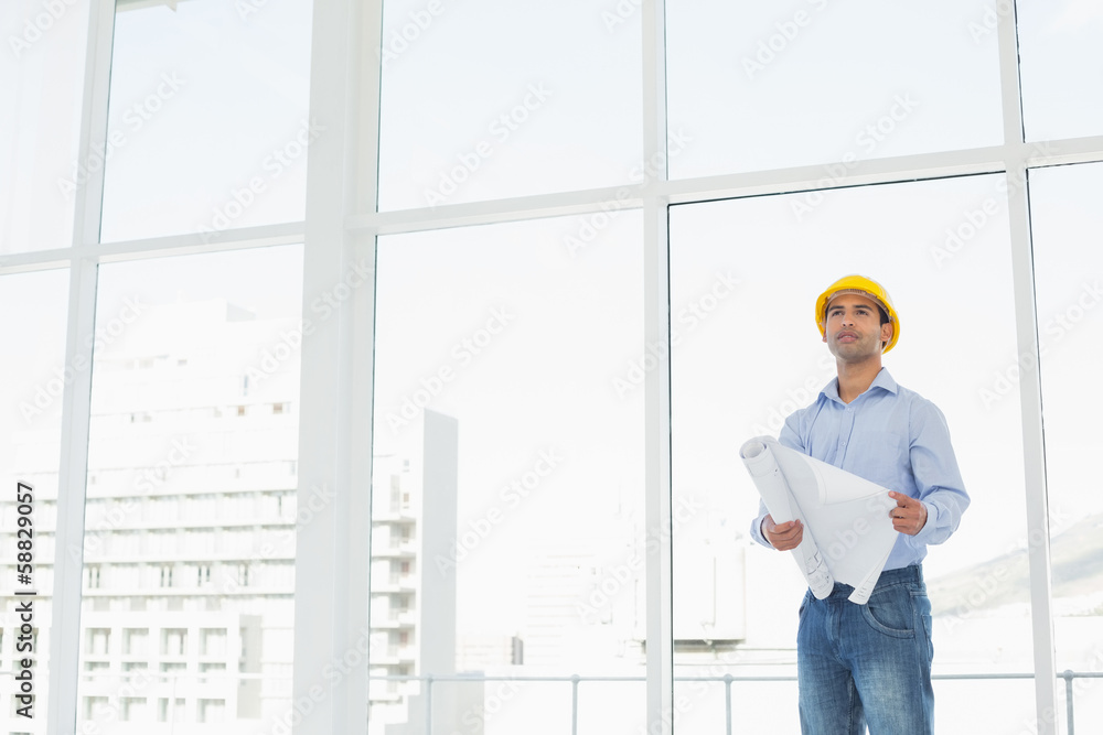 Young architect in yellow hard hat with plans in office Young architect in yellow hard hat with plans in office