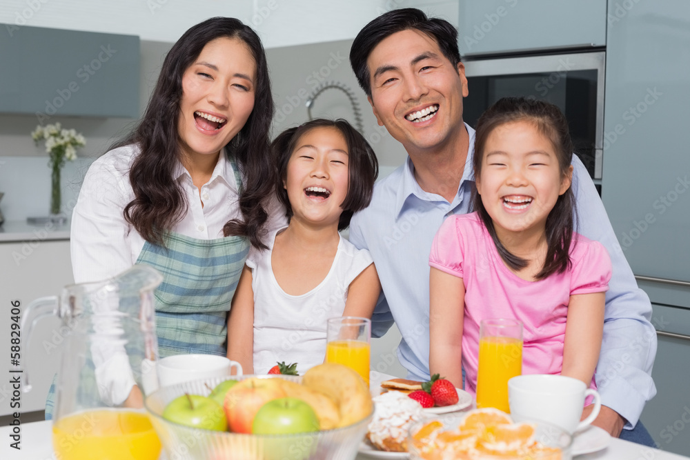 Cheerful family of four enjoying healthy breakfast in kitchen Cheerful family of four enjoying healthy breakfast in kitchen