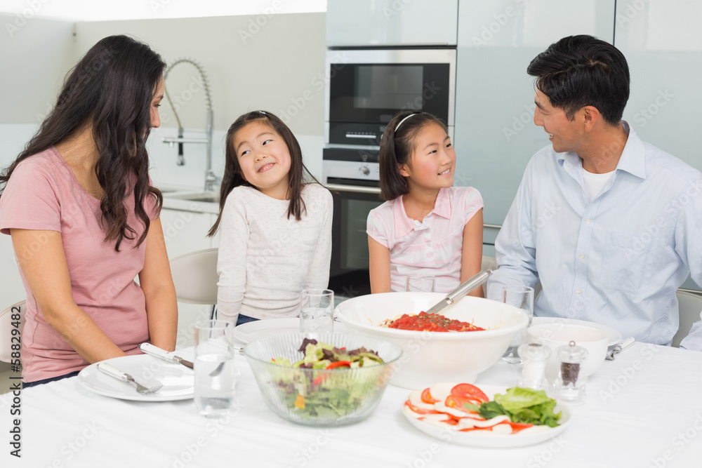Smiling family of four sitting at dining table in kitchen Smiling family of four sitting at dining table in kitchen