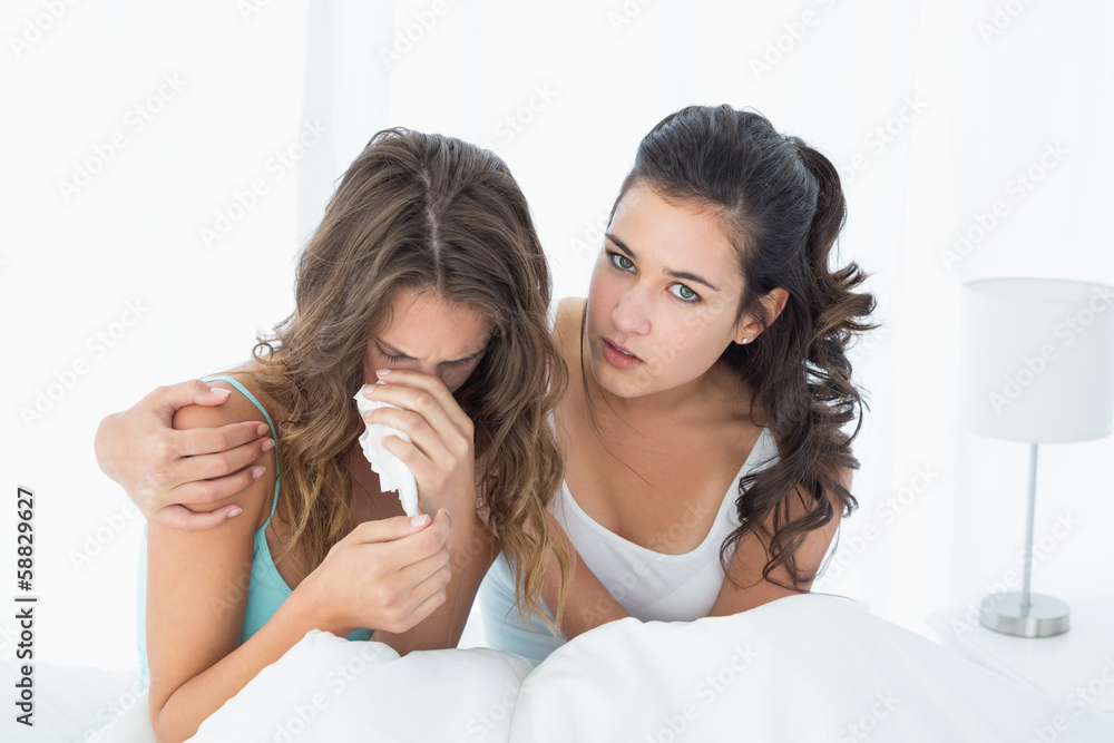 Woman consoling a crying female friend in bed Woman consoling a crying female friend in bed