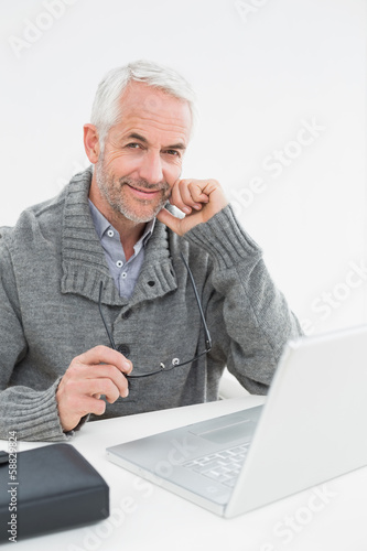 Portrait of a smiling mature man with laptop at desk