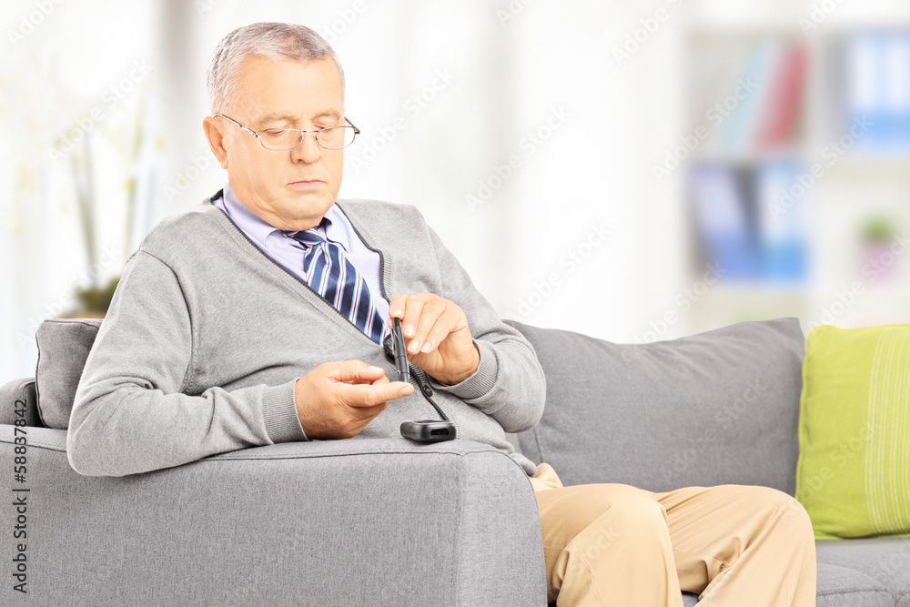 Mature on sofa measuring sugar level in blood using glucometer Mature on sofa measuring sugar level in blood using glucometer