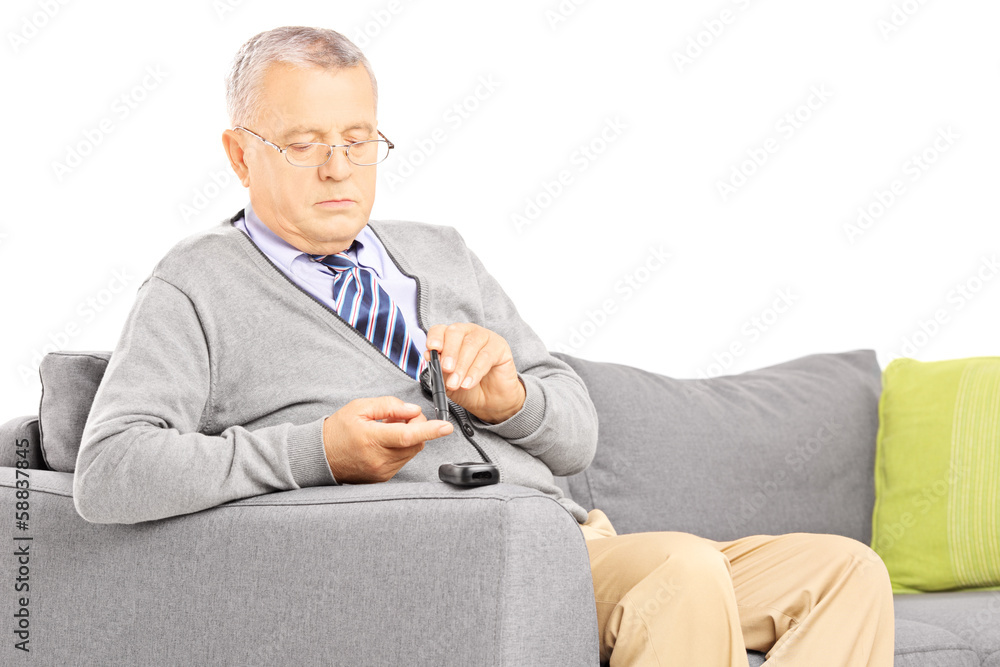 Mature seated on a sofa measuring sugar level in blood Mature seated on a sofa measuring sugar level in blood