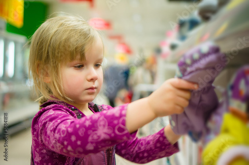 Adorable girl select winter gloves in supermarket