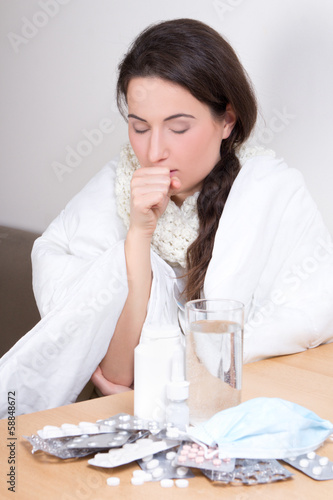 young woman sneezing and pills on the table