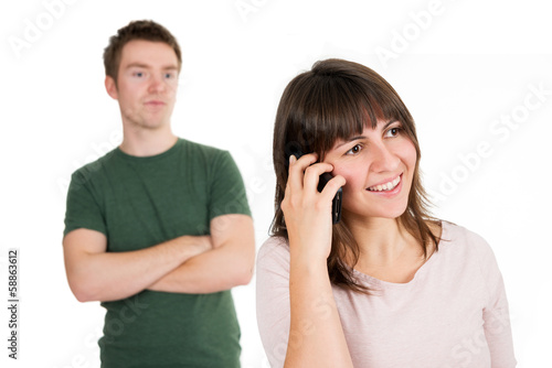 Junge Frau telefoniert lächelnd, Mann genervt im Hintergrund © Kitty