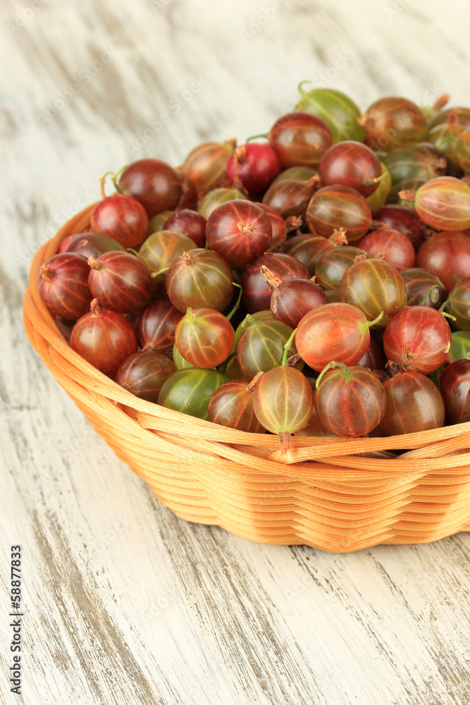 Obraz premium Fresh gooseberries in wicker basket on table close-up