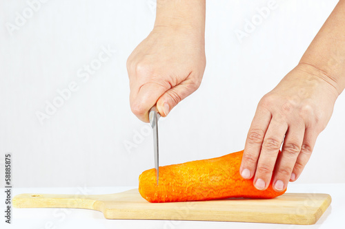 Hand with a knife cuts carrot on a white background