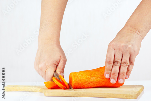 Female hand slices carrots on a white background