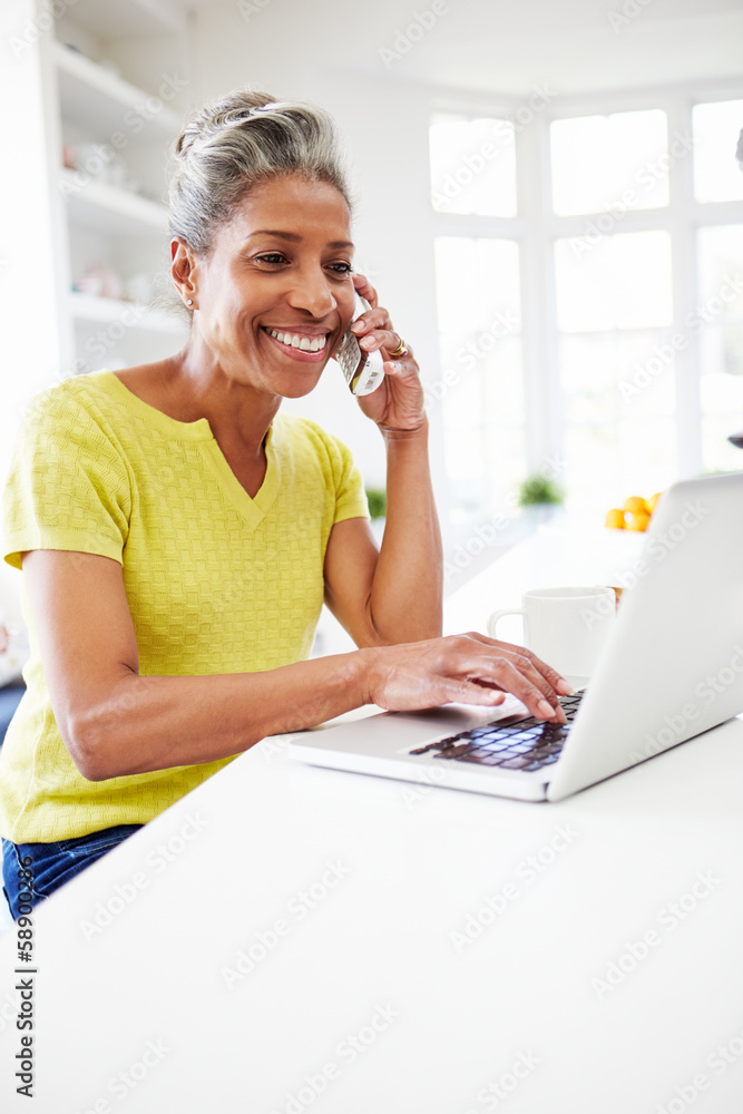 Woman Using Laptop And Talking On Phone In Kitchen At Home Woman Using Laptop And Talking On Phone In Kitchen At Home