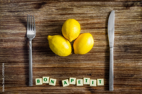 Fotografering Silverware and lemons on wooden table with Bon apetit sign
