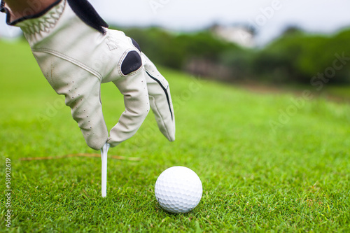 hand placing golf ball on tee over beautiful golf course with