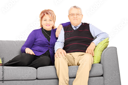 Wife and husband sitting on a modern sofa and looking at camera