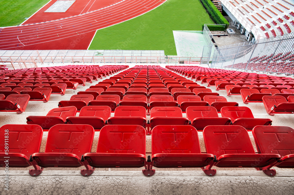 Fototapeta premium Czerwone siedzenia stadionowe z czerwoną bieżnią i zieloną trawą.