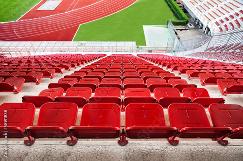 Red stadium seats with red running track & green grass.