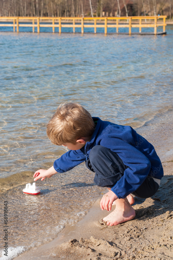 Kleiner Junge spielt am Seeufer mit einem Spielzeugschiff Kleiner Junge spielt am Seeufer mit einem Spielzeugschiff