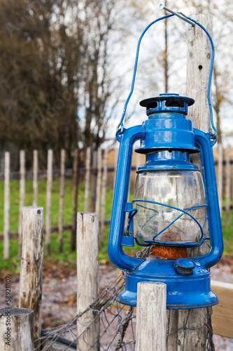 Blue vintage kerosene lamp hangs on wooden outdoor fence © evannovostro