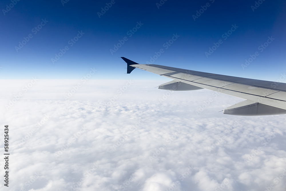 Wing of airplane flying above the clouds in the sky Wing of airplane flying above the clouds in the sky