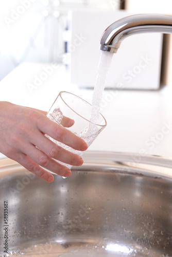 Hand holding glass of water poured from kitchen faucet