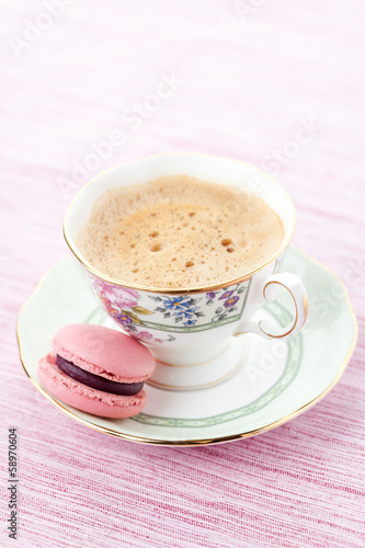 Pink macaroon on a saucer with cup of coffee