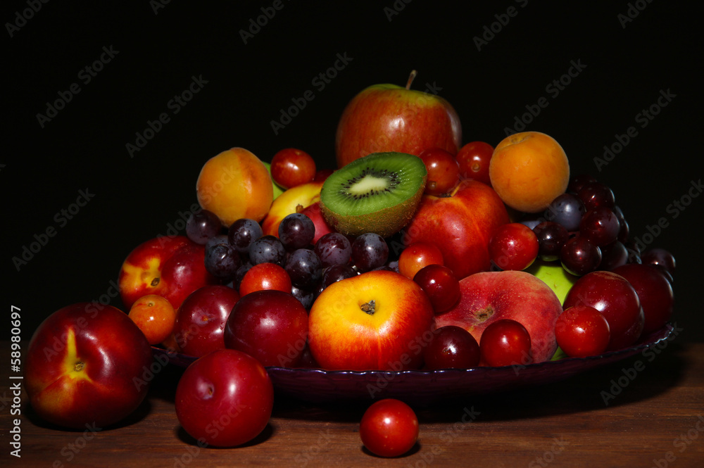 Assortment of juicy fruits on wooden table, on dark background Assortment of juicy fruits on wooden table, on dark background