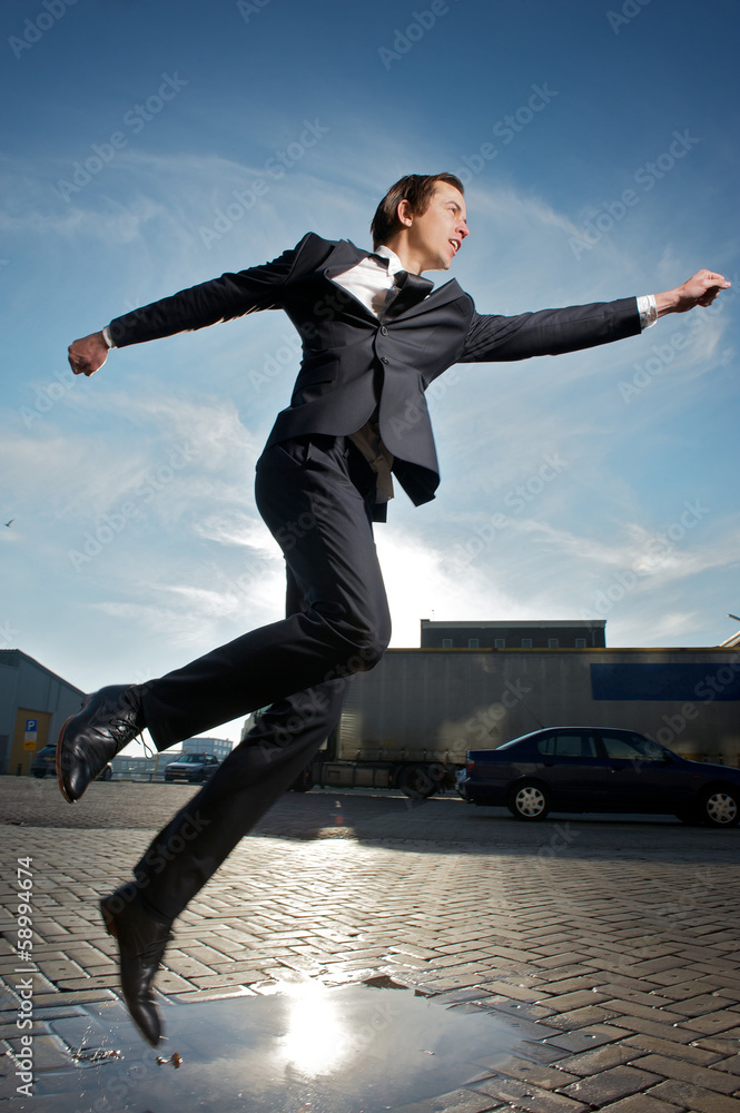 Businessman jumping over puddle of water on the street Businessman jumping over puddle of water on the street