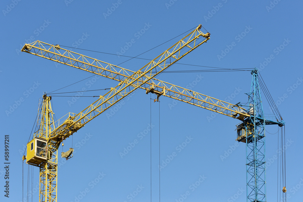 Two building crane yellow and blue visually intersect Two building crane yellow and blue visually intersect