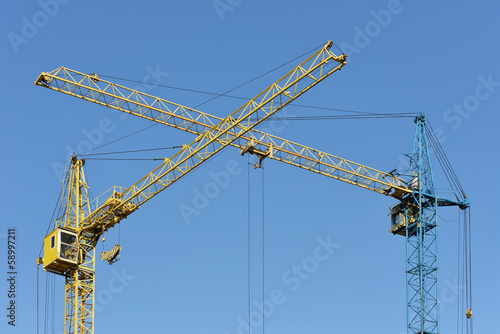 Two building crane yellow and blue visually intersect