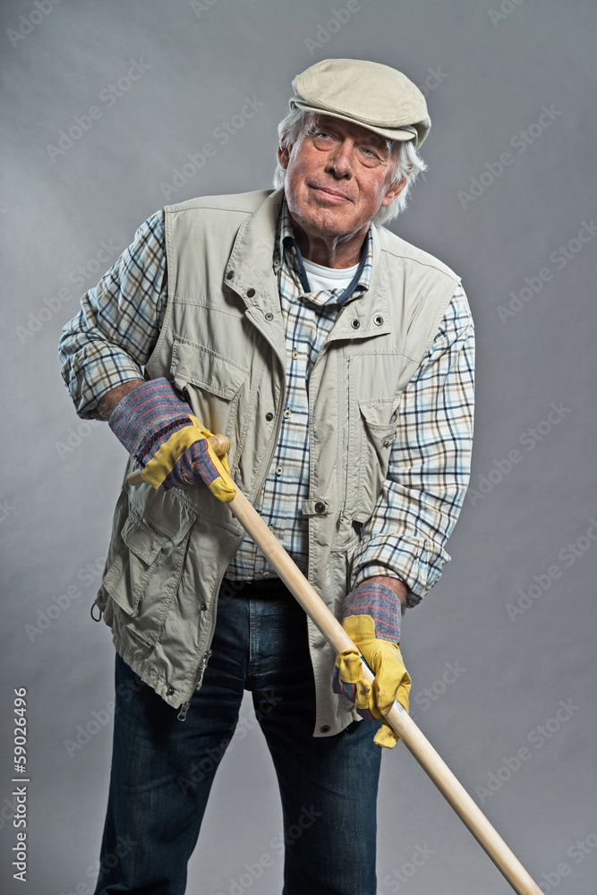 Gardener senior man with hat holding hoe. Studio shot against gr Gardener senior man with hat holding hoe. Studio shot against gr
