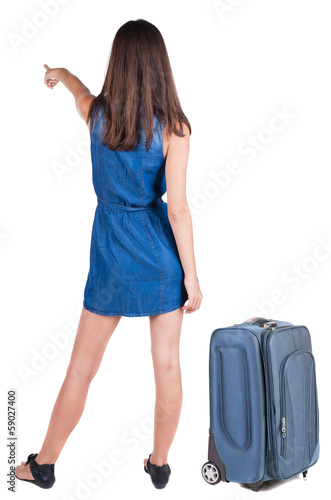 Back view of young brunette woman traveling with suitcas and poi