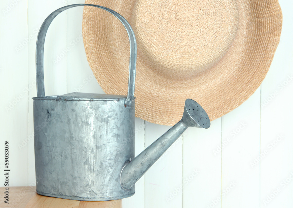 Watering can with hat on wooden background Watering can with hat on wooden background