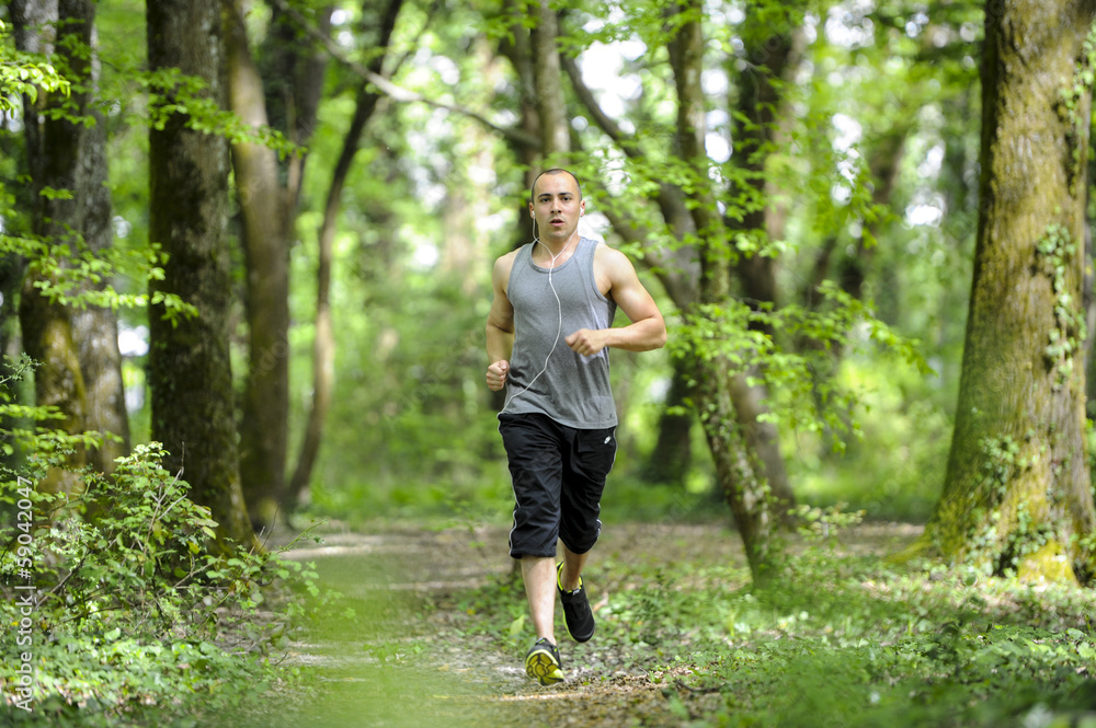 Young man running in the woods listening music