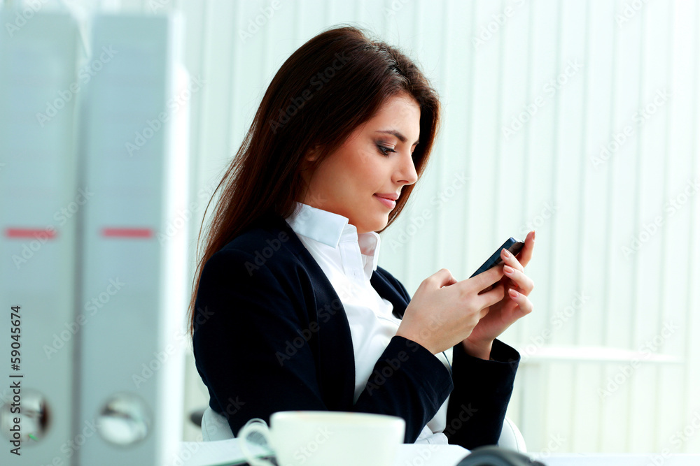 Young beautiful businesswoman typing on her smartphone in office Young beautiful businesswoman typing on her smartphone in office