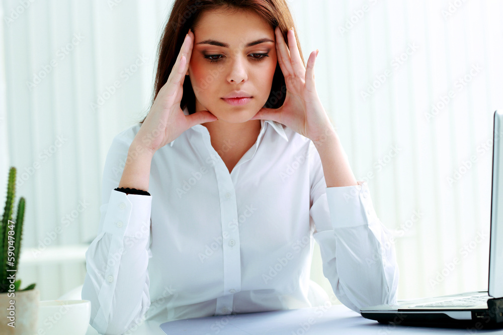 Young pensive businesswoman sitting at the table in office Young pensive businesswoman sitting at the table in office