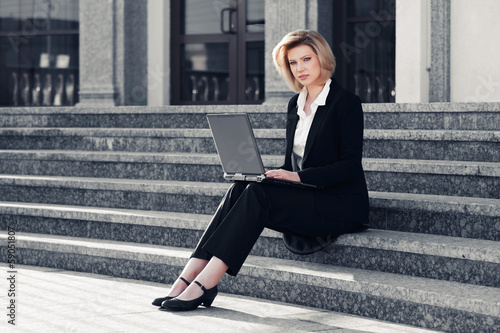 Blond business woman using laptop on the steps